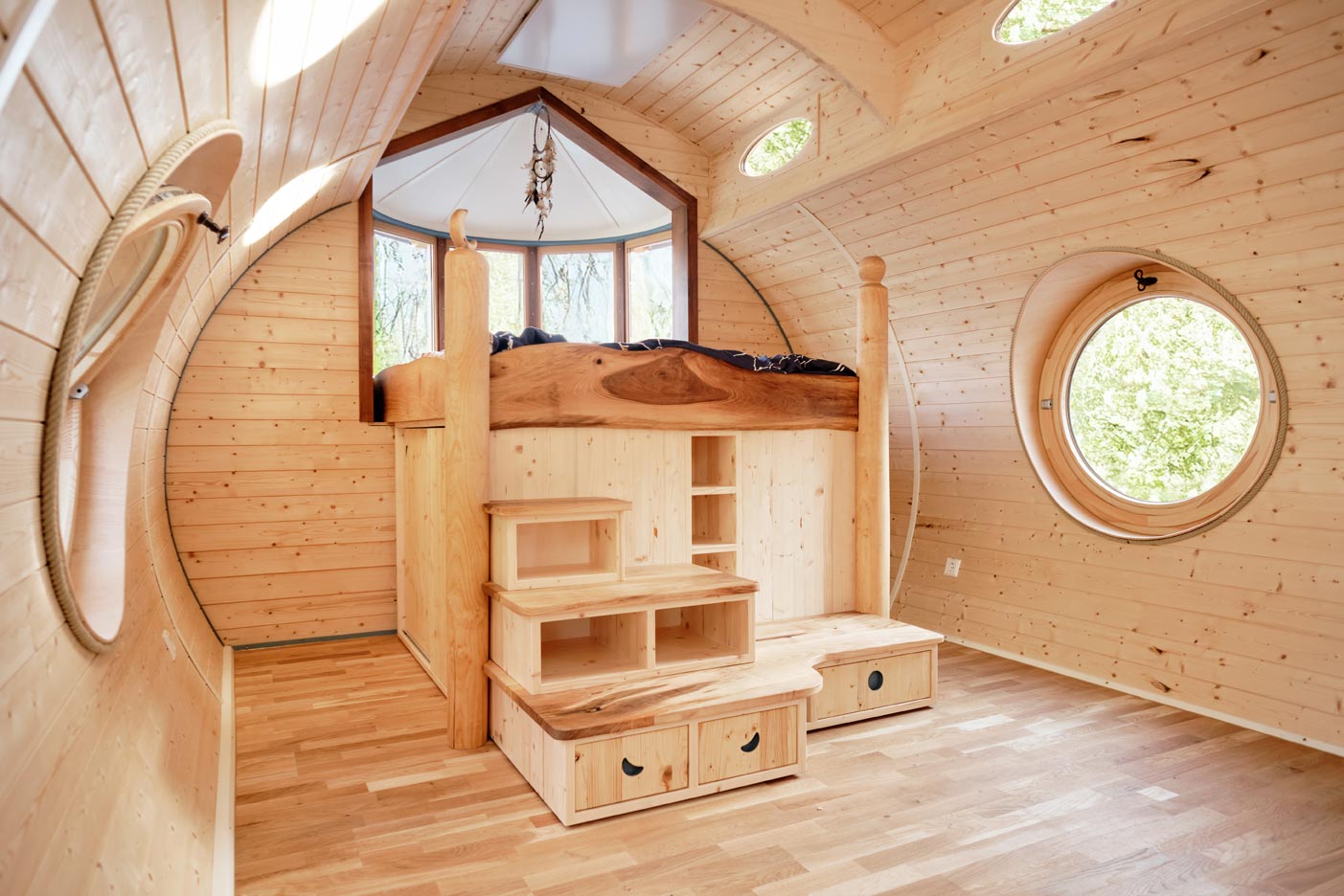 Schlafbereich im Holzwagen: Hochbett aus Massivholz mit Stufen, Stauraum und runden Fenstern.