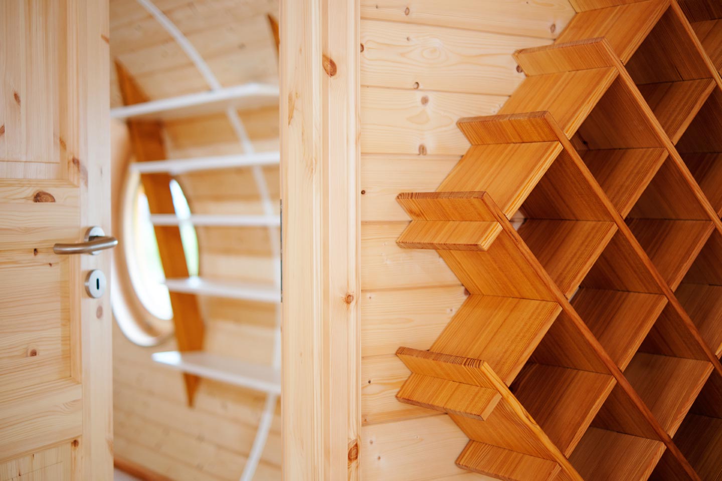 Garderobenbereich im Holzwagen mit rundem Fenster, weißer Bank-/Hakenleiste und Holzregal.